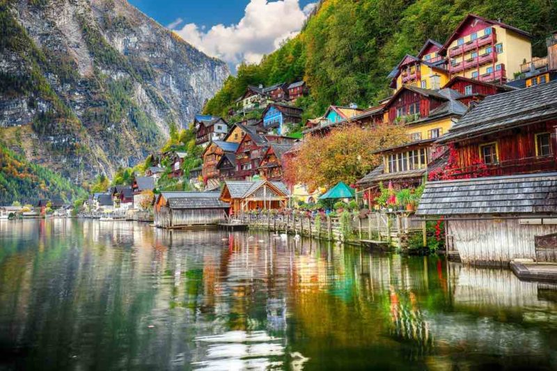 Sunny autumnal day at famous Hallstatt lakeside town reflecting in Hallstattersee lake.